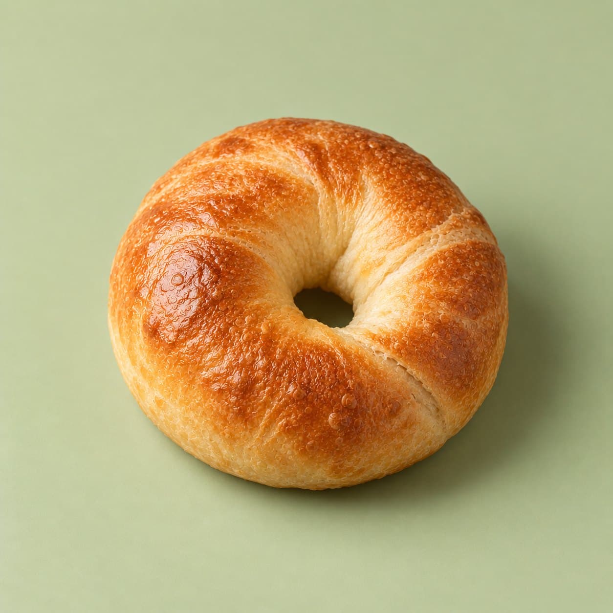 A golden New York–style bagel from bōm dough on a pale green background.