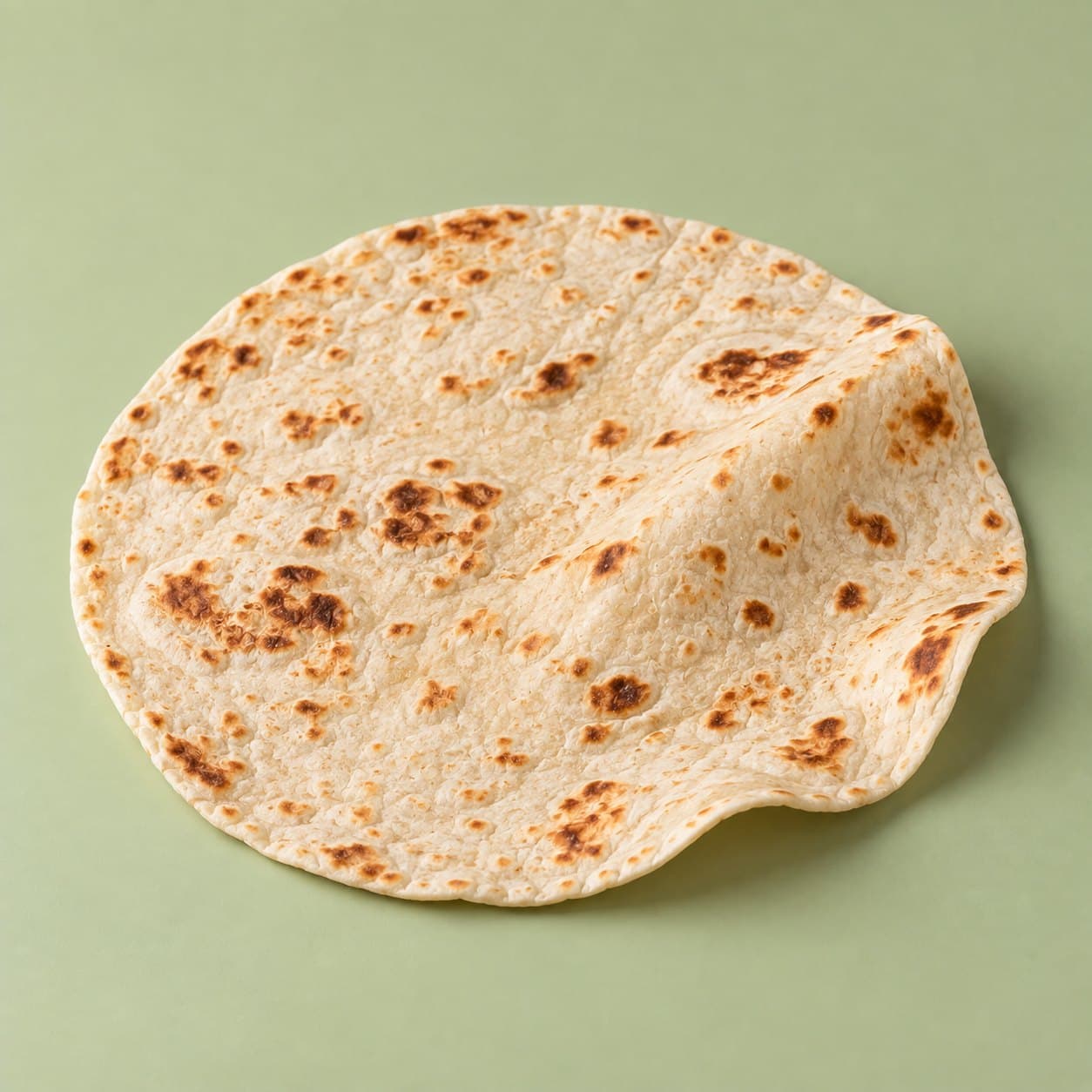 A gluten-free flour tortilla with toasted brown spots, the base of the bōm-rrito, on a pale green background.