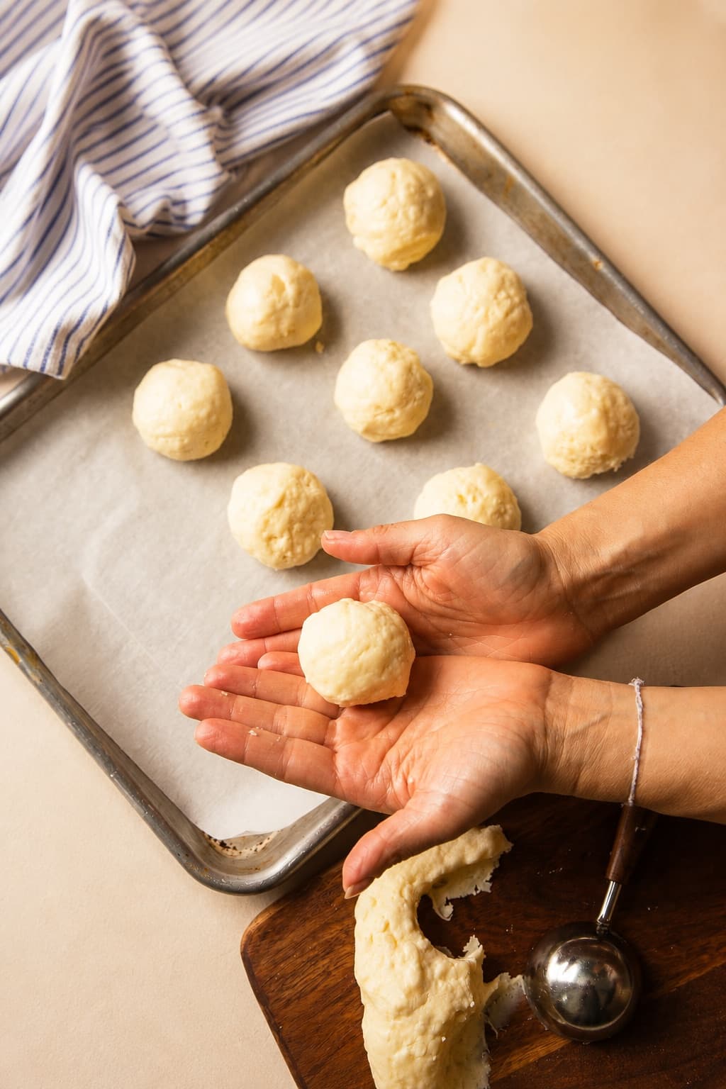 Hands rolling bōm dough pão de queijo dough into balls on a parchment-lined baking tray — naturally gluten-free Brazilian cheese bread, made fresh by hand.