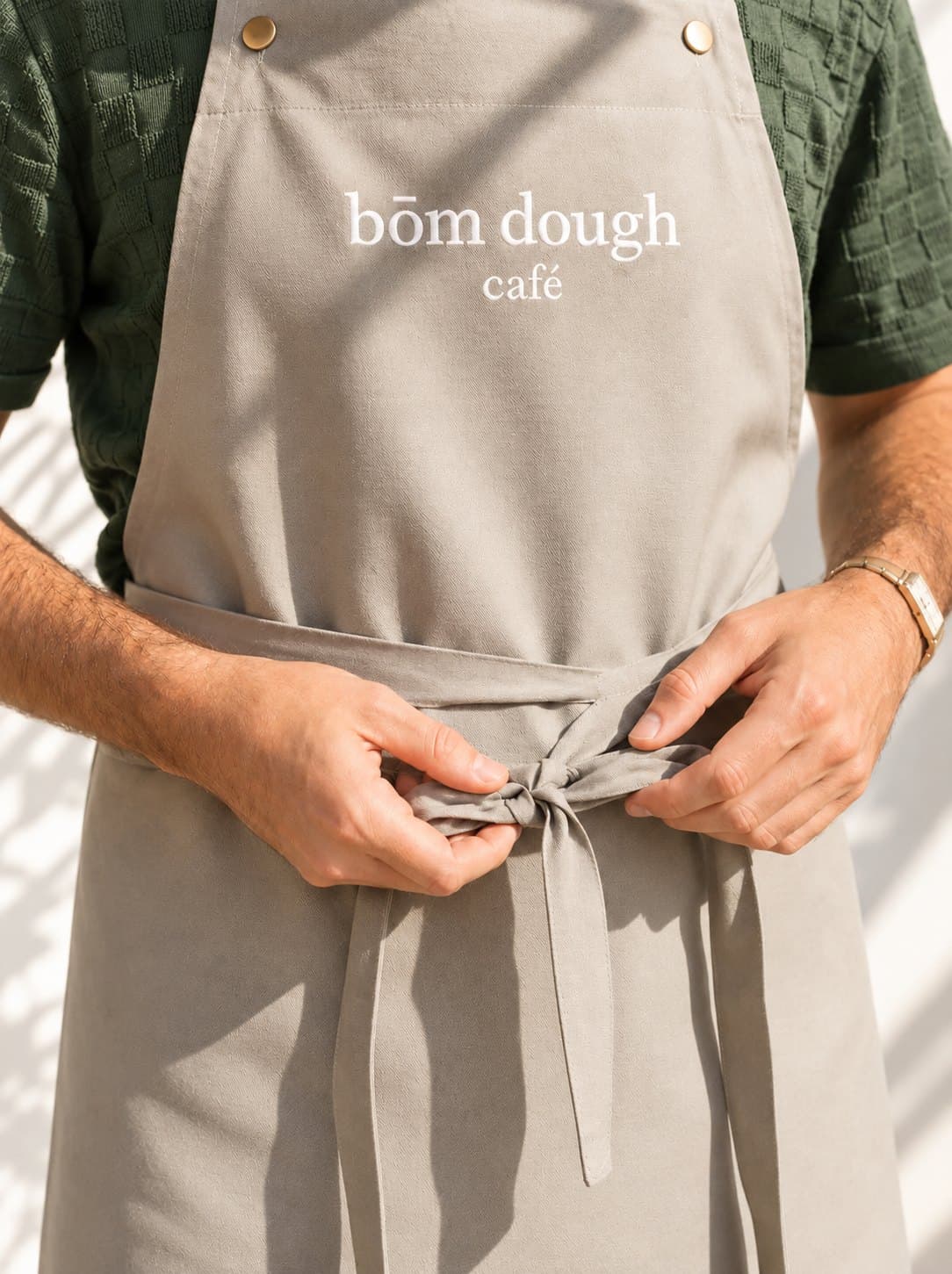 bōm dough team — bakers and baristas, Cambridge, MA A bōm dough baker tying on a grey bōm dough café apron in Cambridge, MA.