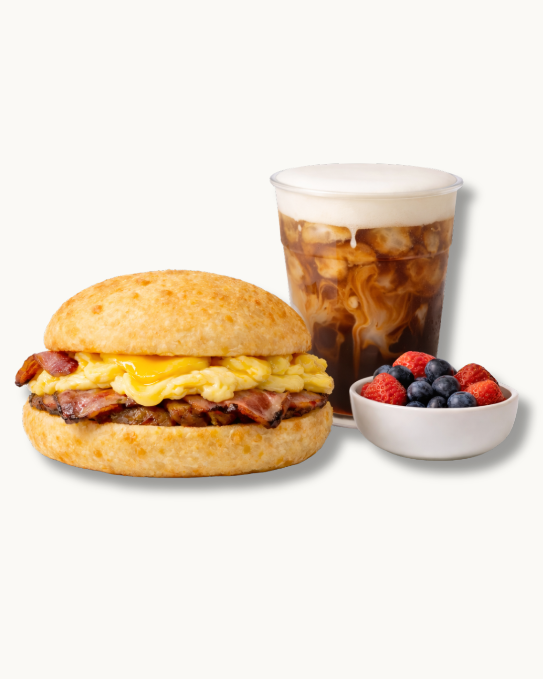 breakfast sandwich on a pão de queijo bun with bacon, scrambled eggs, white cheese, cold brew with cold foam, and fresh berries
